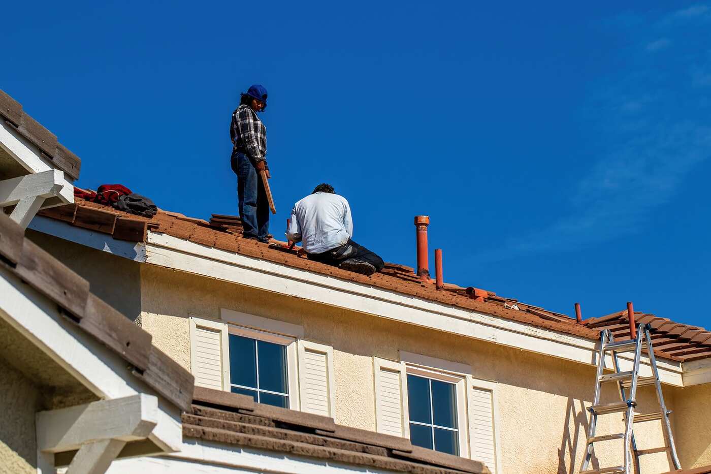 Workers on a tiled roof under a clear sky