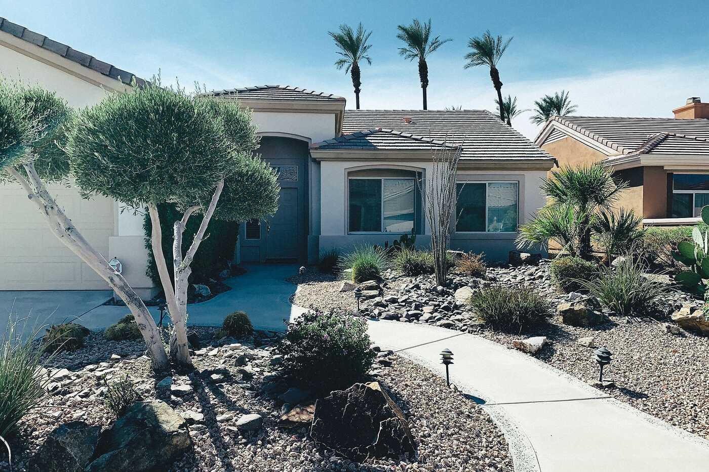A single-story home with palms and gravel landscaping